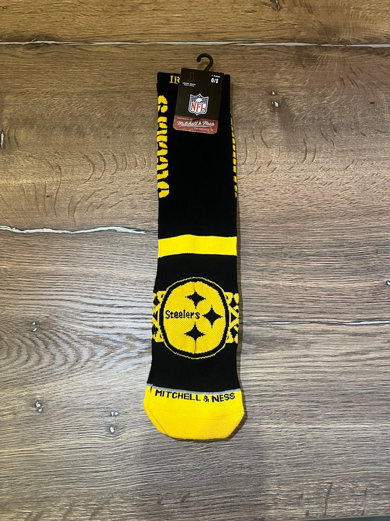Steelers Socks from Pittsburgh Steelers Europe Shop, featuring team colors and logo, plus “Steelers” and “MITCHELL & NESS” text, shown in packaging on a wooden floor.