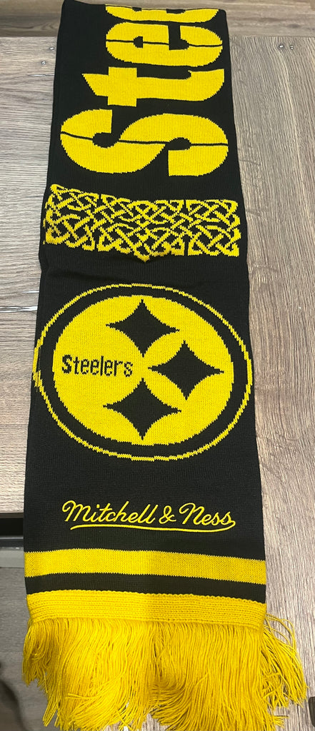 The Scarf Color Rush Scarf by Pittsburgh Steelers Europe Shop features black and yellow colors, the team logo, “Steelers” text, patterns, and “Mitchell & Ness” embroidery, shown on a wooden surface.