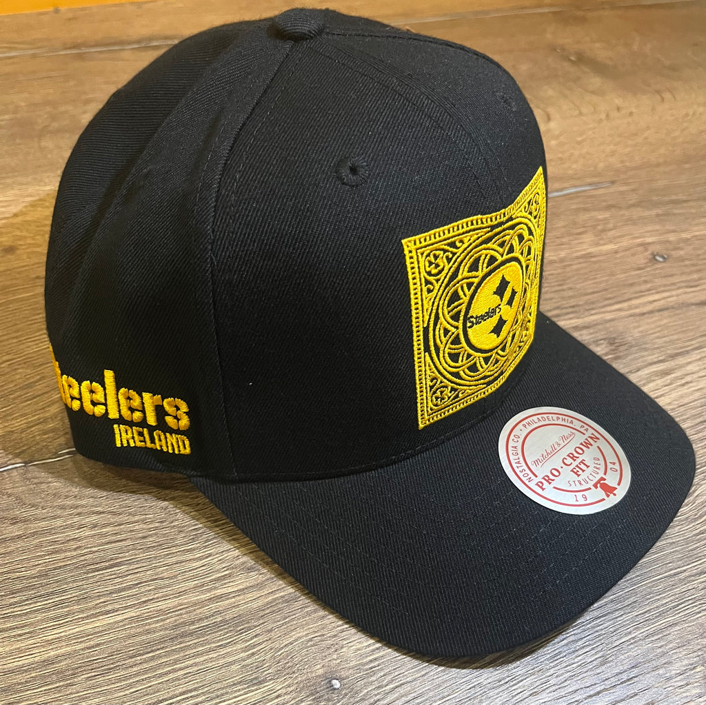 The Steelers Pro Crown Logo Hat from Pittsburgh Steelers Europe Shop is a black cap with a yellow logo patch on the front and "Steelers Ireland" embroidered on the side, displayed on a wooden surface.