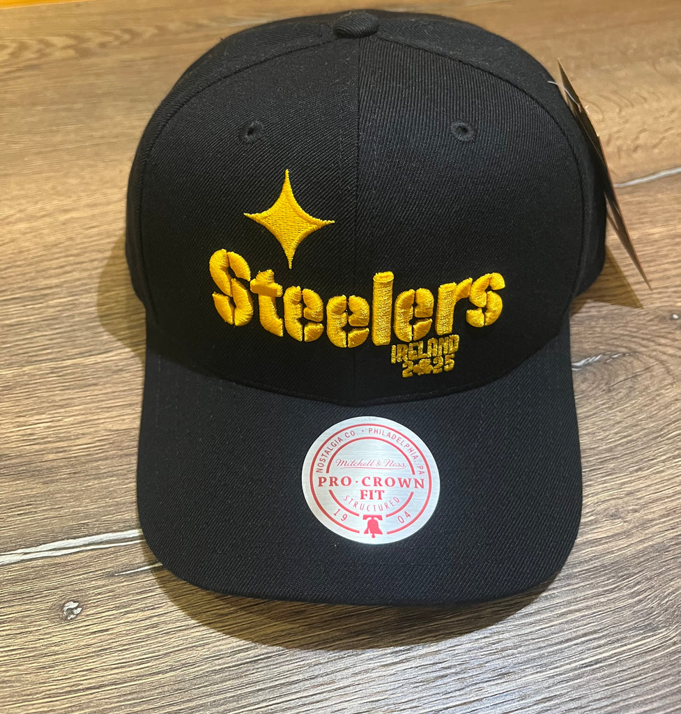 The Hat Pro Crown Wordmark by Pittsburgh Steelers Europe Shop features a black design with an embroidered yellow starburst logo on the front and a PRO CROWN FIT sticker on the brim, displayed on a wooden surface.