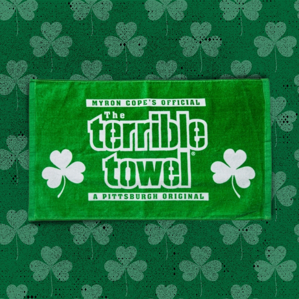 A green Terrible Towel with white text and shamrock graphics reads Myron Cope’s Official The Terrible Towel, A Pittsburgh Original against a green background with a shamrock pattern.