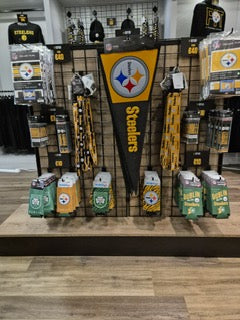 Display of Pittsburgh Steelers merchandise including a large pennant, lanyards, and various accessories in black and gold, arranged on shelves and racks in a store.